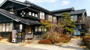 A traditional Japanese building with a dark facade, tiled roof, and a small outdoor seating area with a vending machine.