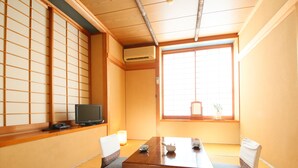A traditional Japanese room with tatami flooring, a low table, cushions, a television, and a window with a view. - Fukashiso (Matsumoto)