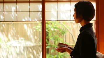A person holding a cup, standing in front of a window with a view of greenery.