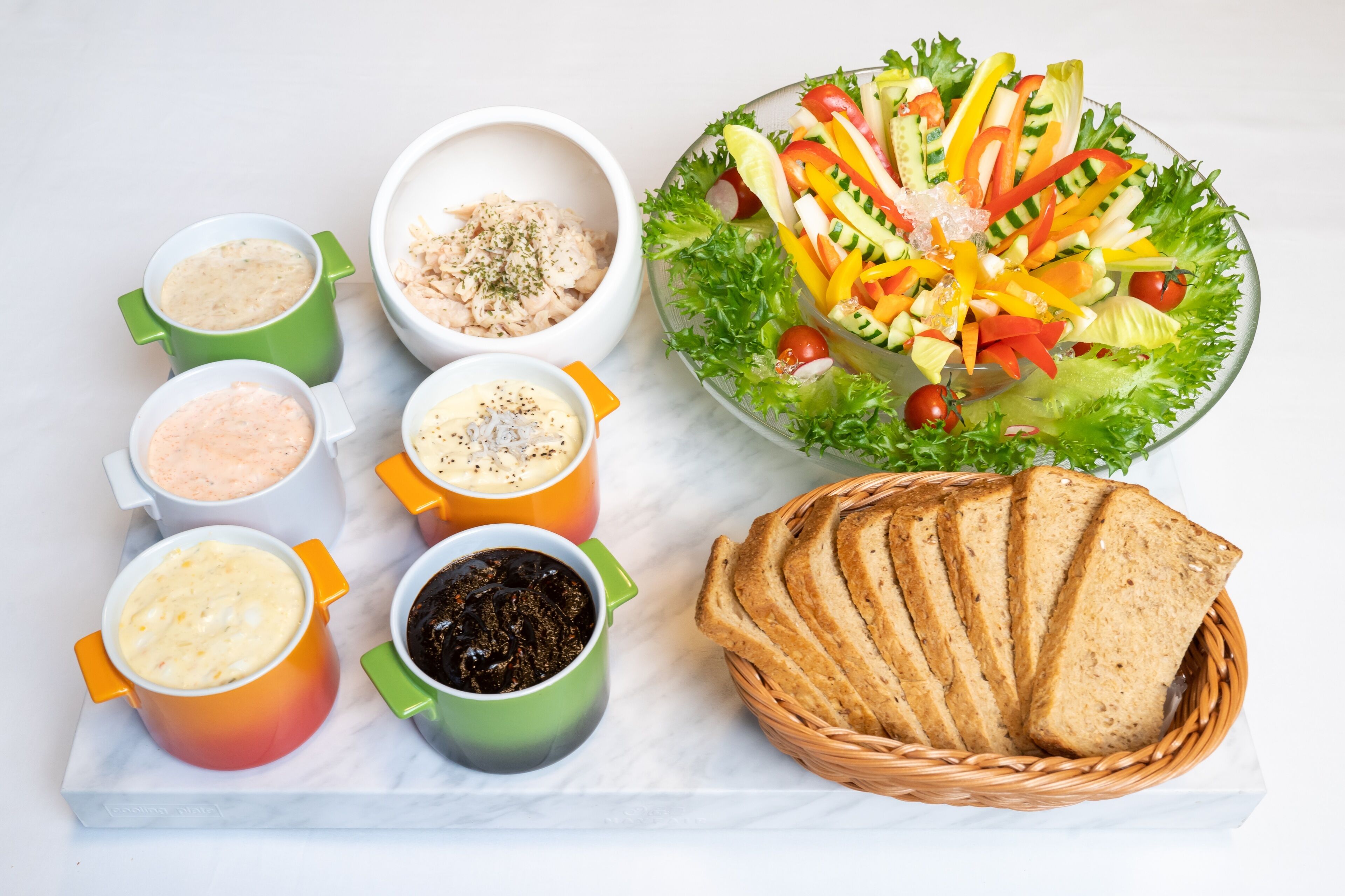 Ein Tisch mit verschiedenen Speisen, darunter Salat, Brot und mehrere kleine Schälchen mit Dips.