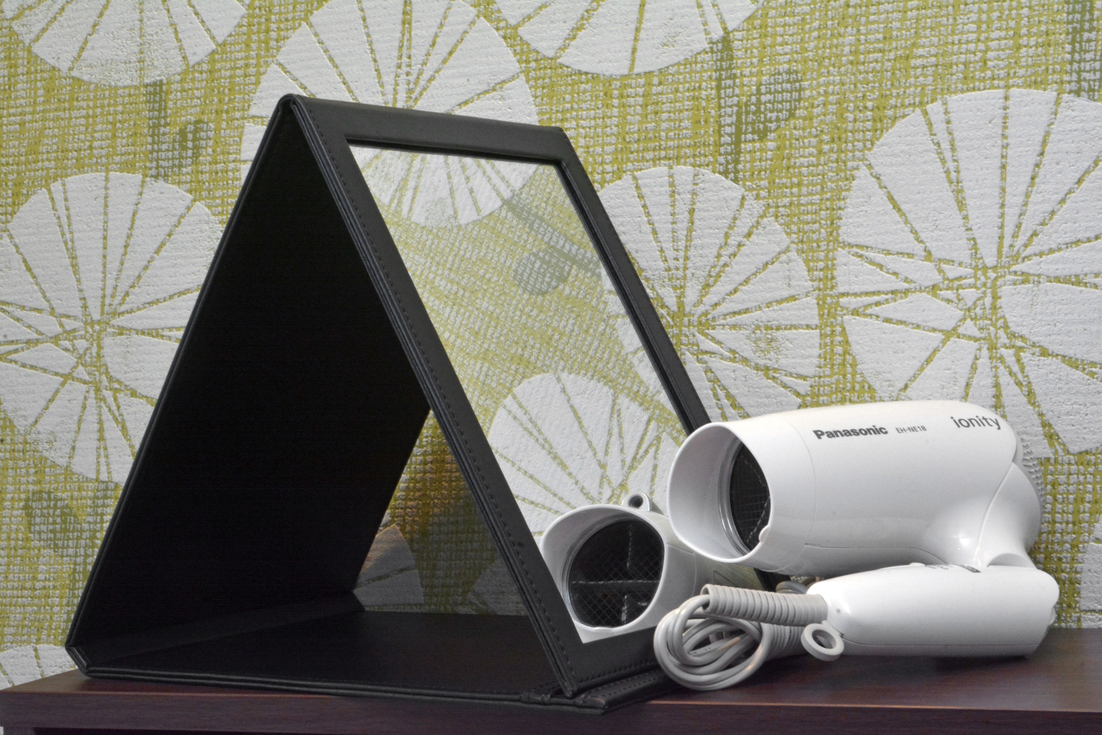A Panasonic hair dryer and a black frame on a wooden surface against a patterned wallpaper.