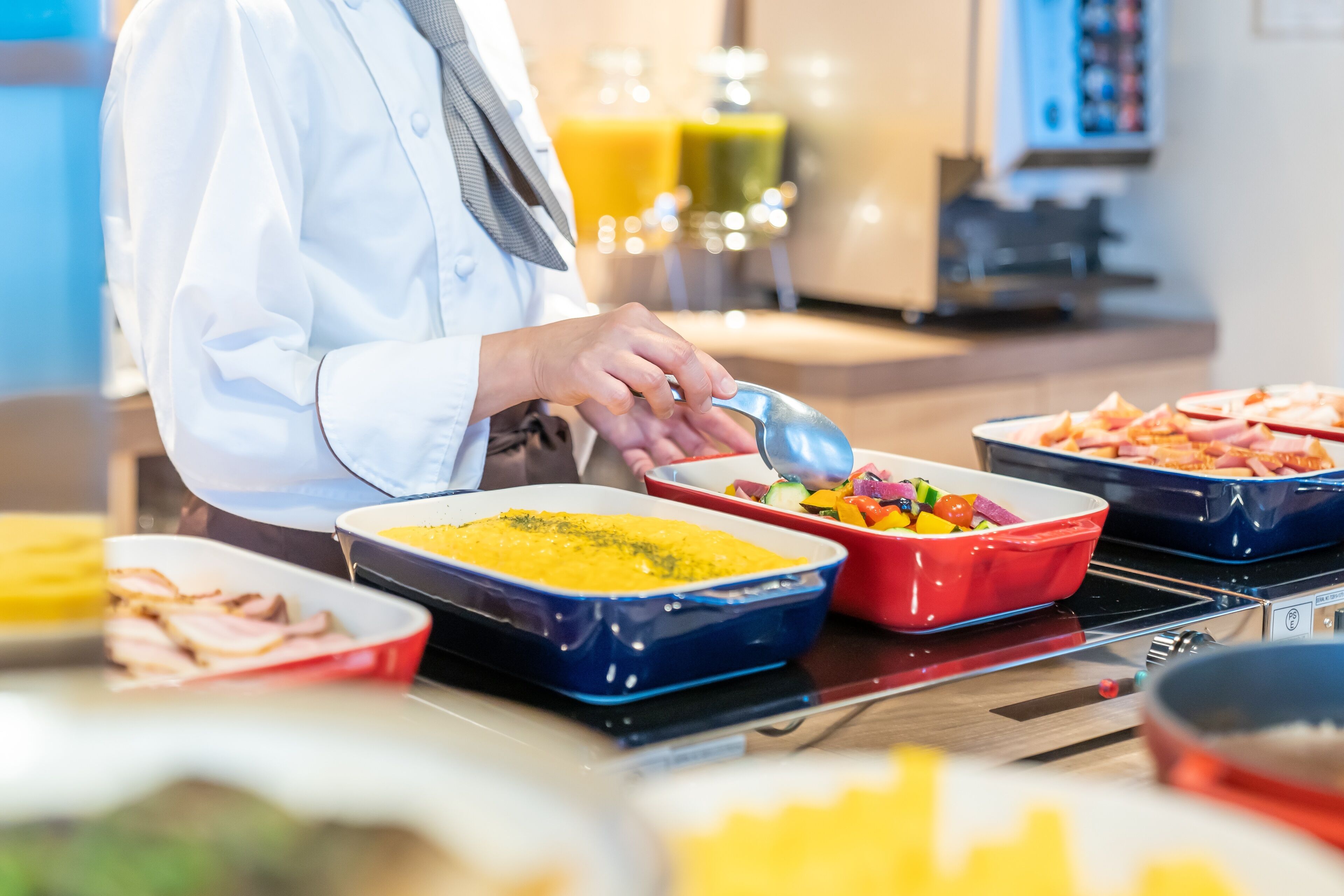 A buffet setup with various dishes in blue and red serving dishes, including a yellow dish and a red dish with vegetables.