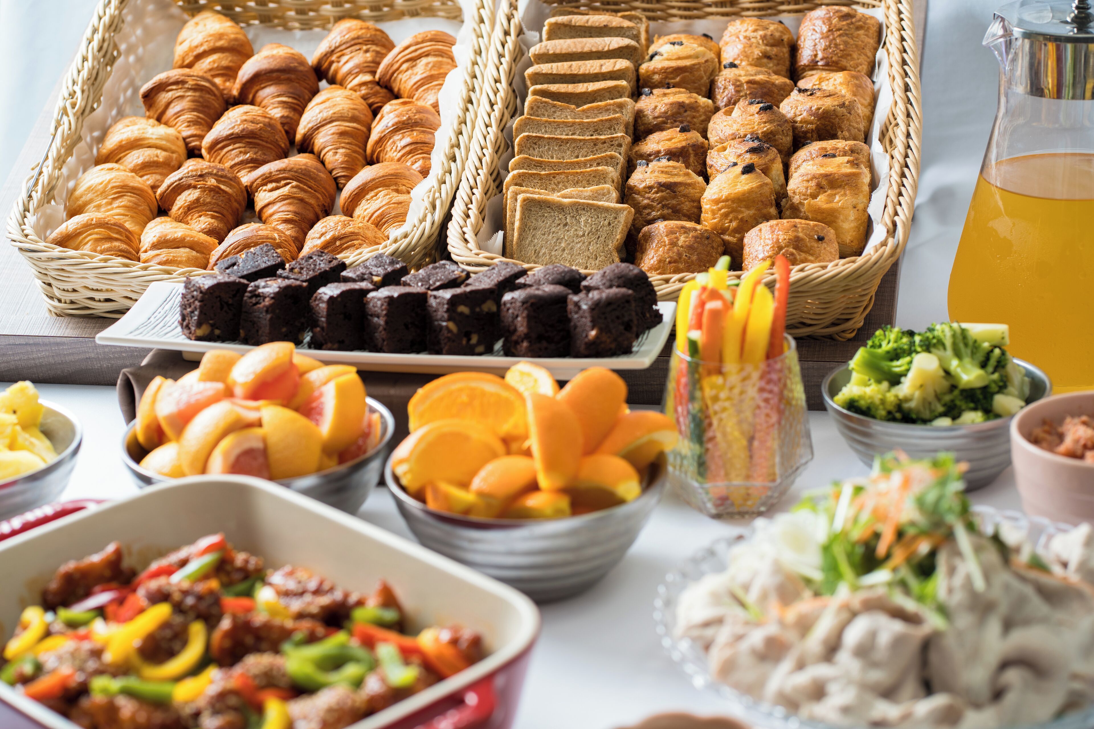 A buffet with various food items including pastries, bread, fruits, and salads.