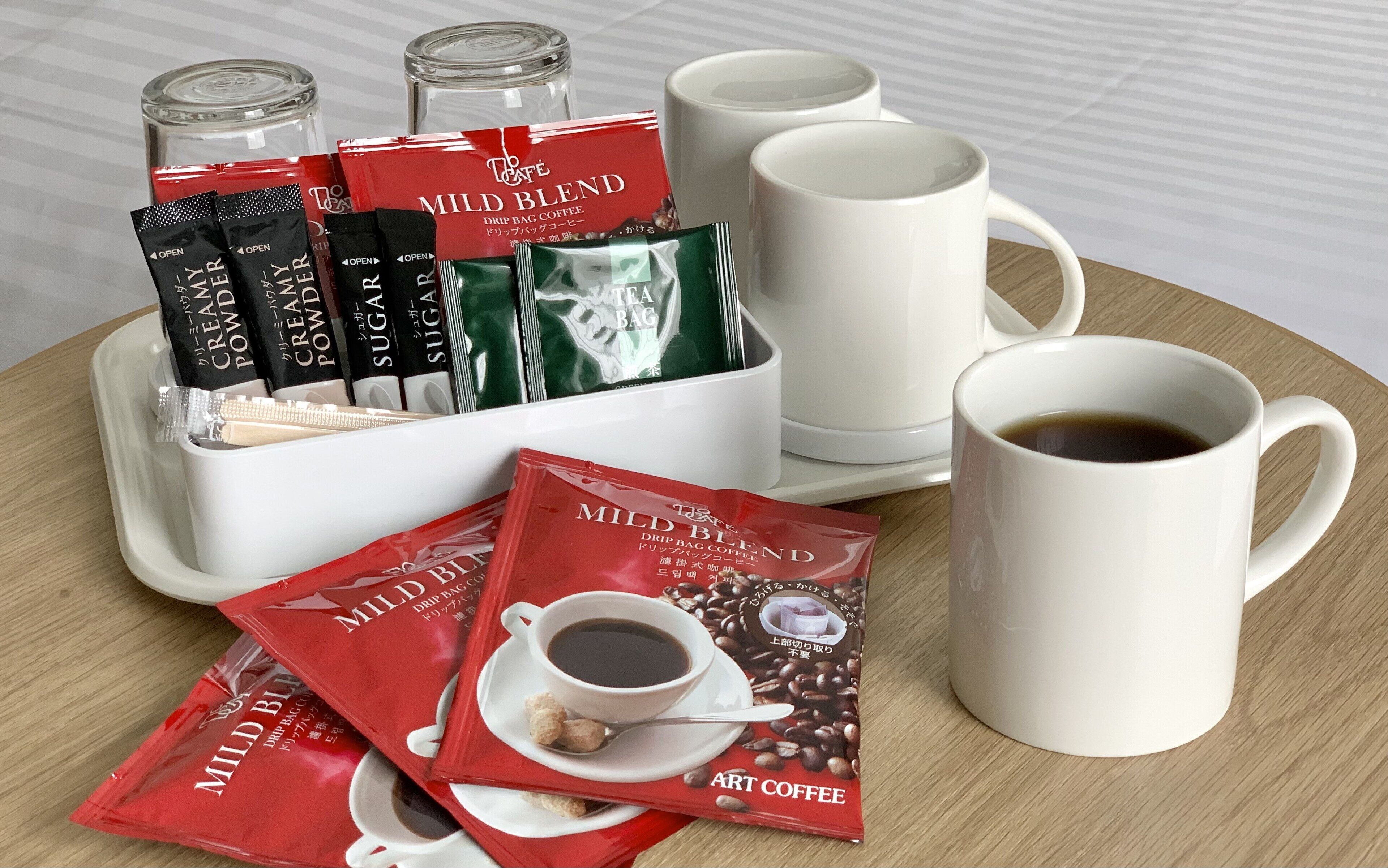 Eine Kaffeestation mit einer weißen Tasse, einer Kaffeekanne und Packungen 'Mild Blend' Filterkaffee.