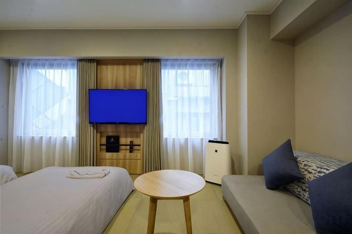 A hotel room with two beds, a TV, a sofa, and a small table.