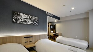 Een hotelkamer met twee bedden, een bureau en een stoel. Aan de muur hangt een groot zwart-wit kunstwerk.