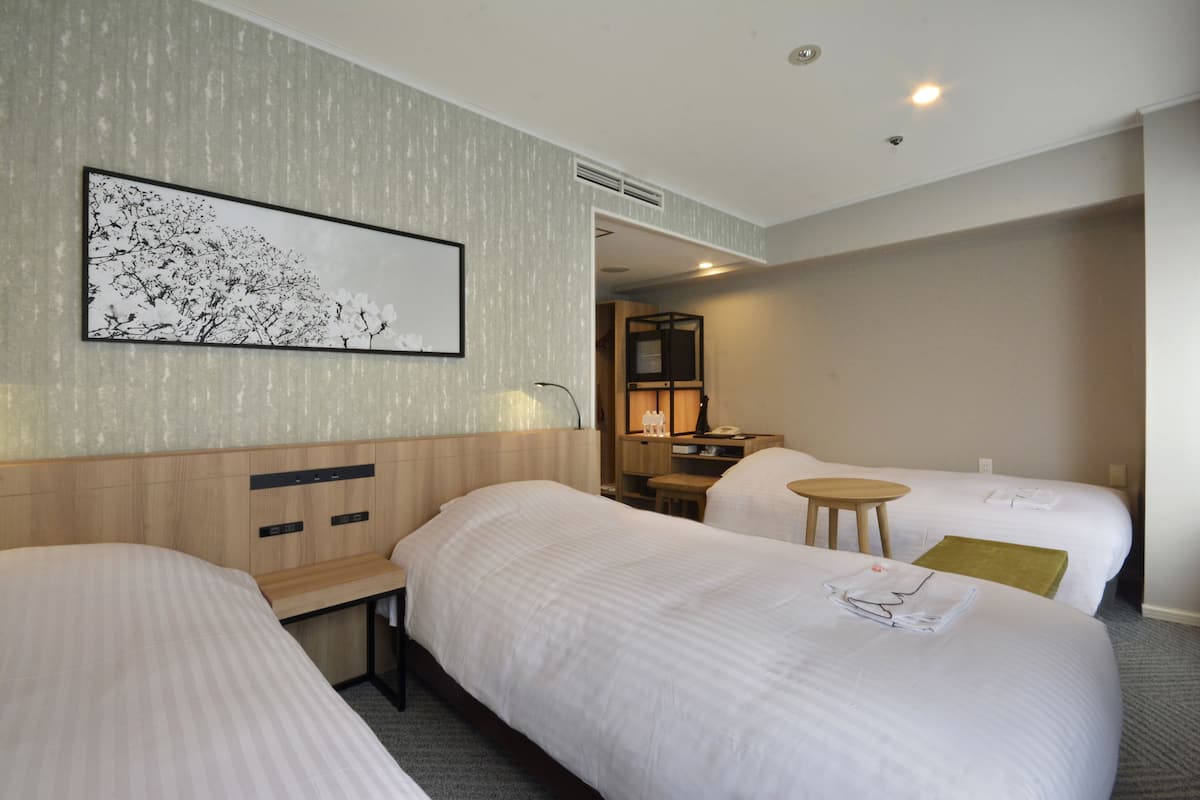 A hotel room with two beds, a wooden headboard, a bedside table, a small round table, a lamp, and a framed picture on the wall.