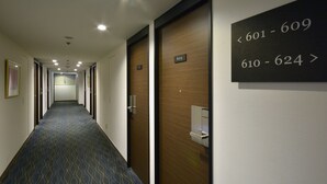 Een hotelgangen met genummerde deuren, een kamerbreed tapijt en een plafond met inbouwspots.