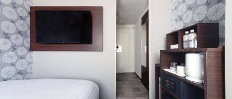 A hotel room with a bed, a flat-screen TV mounted on the wall, a coffee machine, and a mini-fridge.