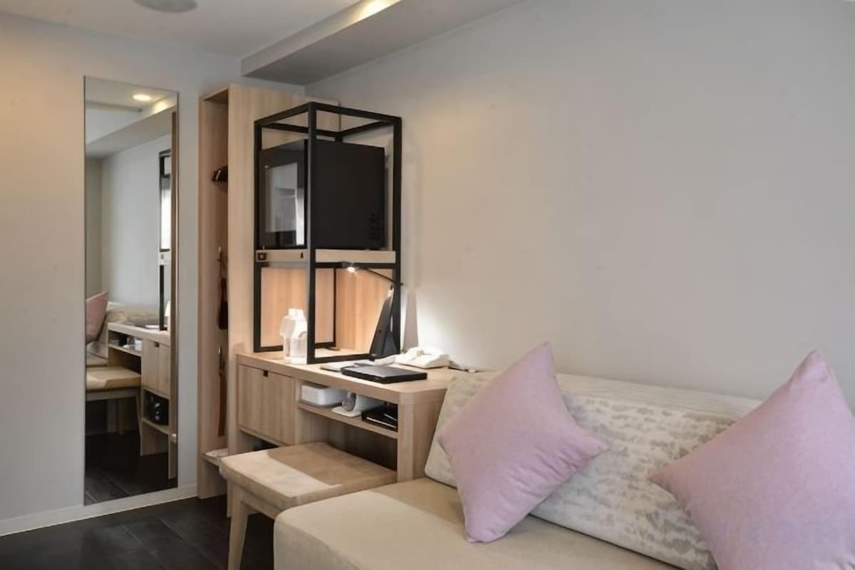 A bedroom with a bed, a desk, a mirror, and a television.