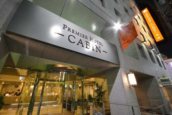 Exterior del Hotel Premier Cabin con puerta giratoria de vidrio y un cartel con el nombre.