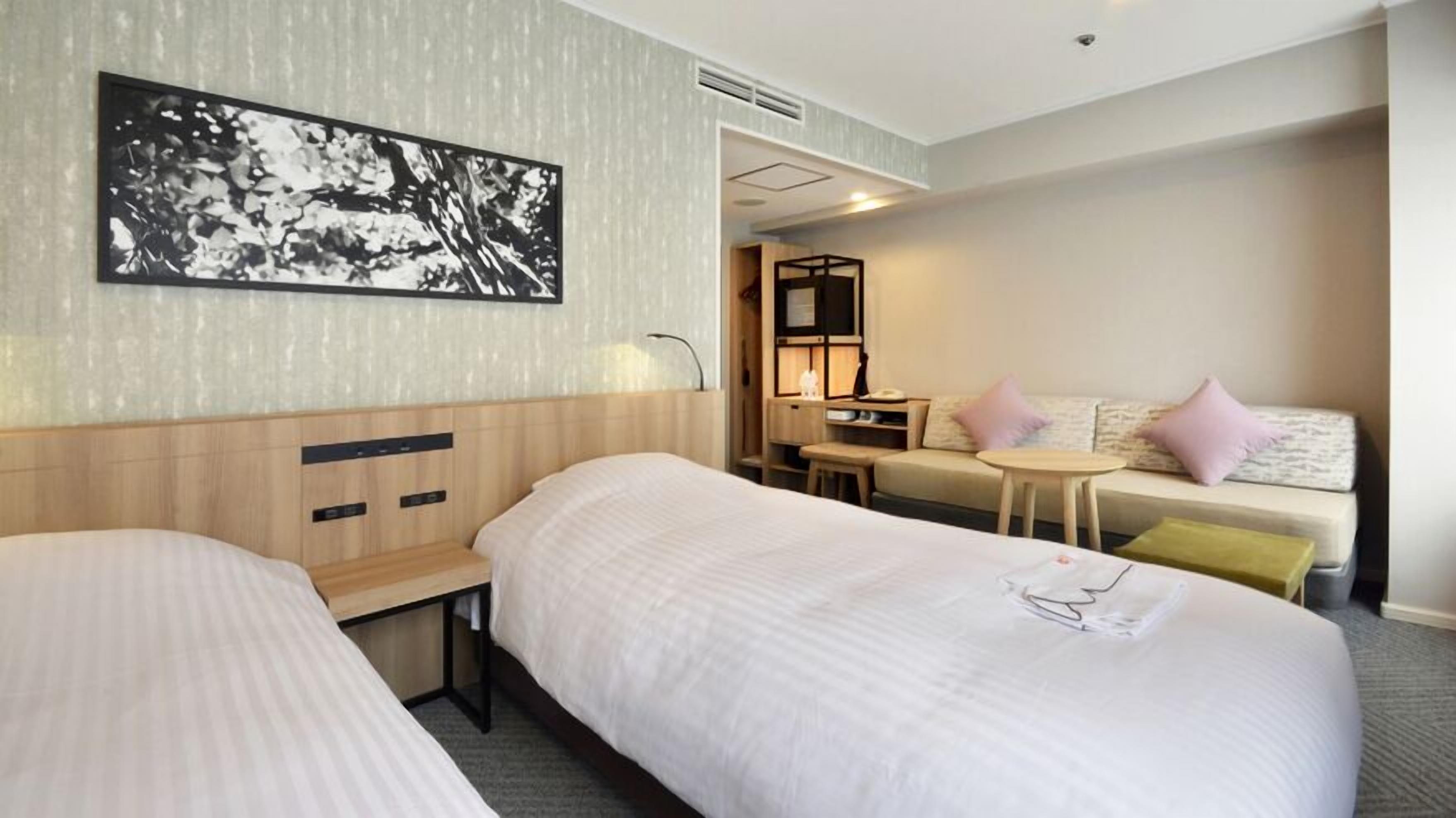 A hotel room with two beds, a desk, a sofa, and a wall-mounted picture.
