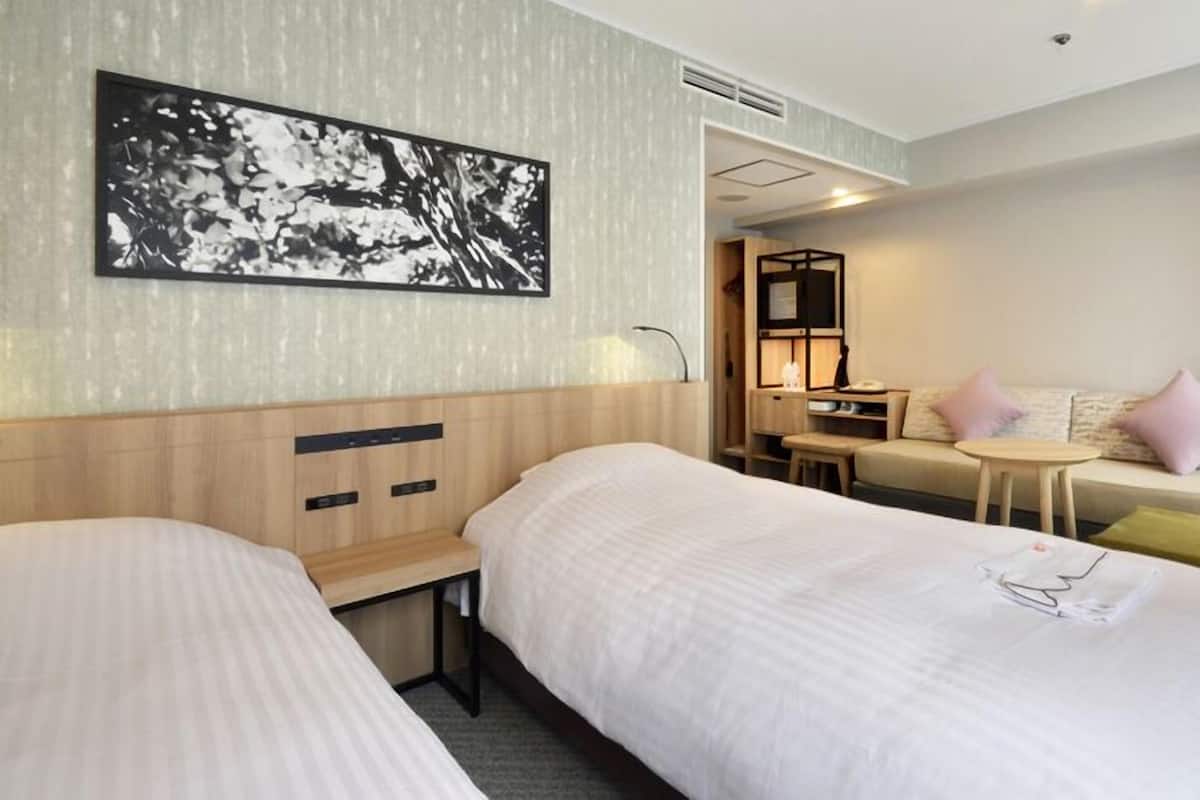 A hotel room with two beds, a desk, a sofa, and a wall-mounted picture.