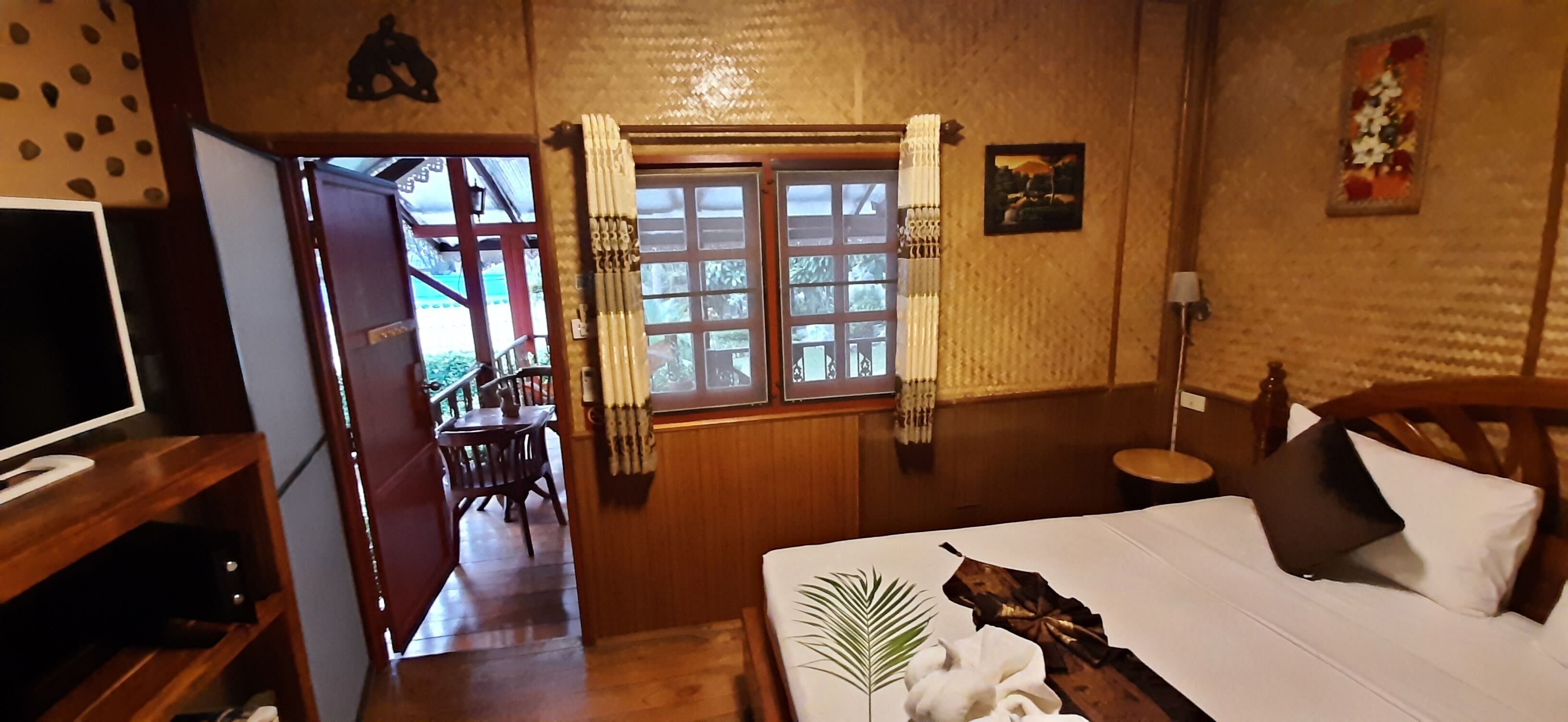 Habitación de hotel con cama, televisión, escritorio de madera, silla, ventana con cortinas y una mesita.