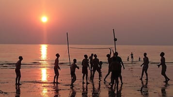 Ein Strandbild, das Personen beim Volleyballspielen bei Sonnenuntergang zeigt.