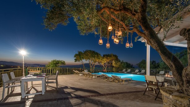 An outdoor pool area with lounge chairs, a table, and hanging lights. - Lofos Soilis (Zakynthos)