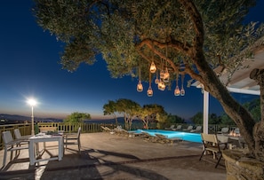 An outdoor pool area with lounge chairs, a table, and hanging lights. - Lofos Soilis (Zakynthos)