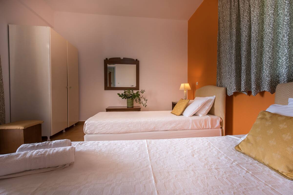 A hotel room with two beds, a nightstand with a lamp, a mirror, and a window with curtains.