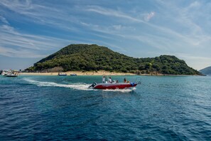 A boat on a calm sea with a beach and a forested hill in the background. - Lofos Soilis (Zakynthos)