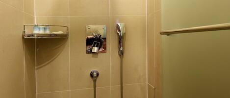 A shower with a handheld showerhead, a wall-mounted control panel, and a glass shelf with toiletries.