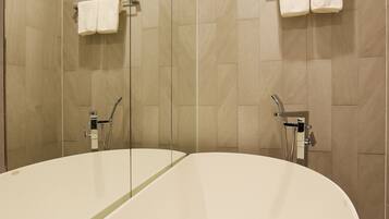 A modern bathroom with a large oval bathtub, a glass-enclosed shower, and beige tiled walls.