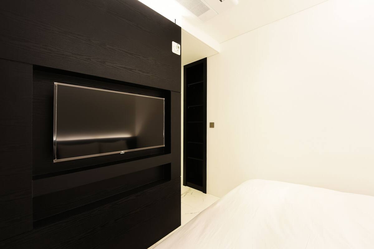 A modern hotel room with a built-in TV, a bed, and a wardrobe.