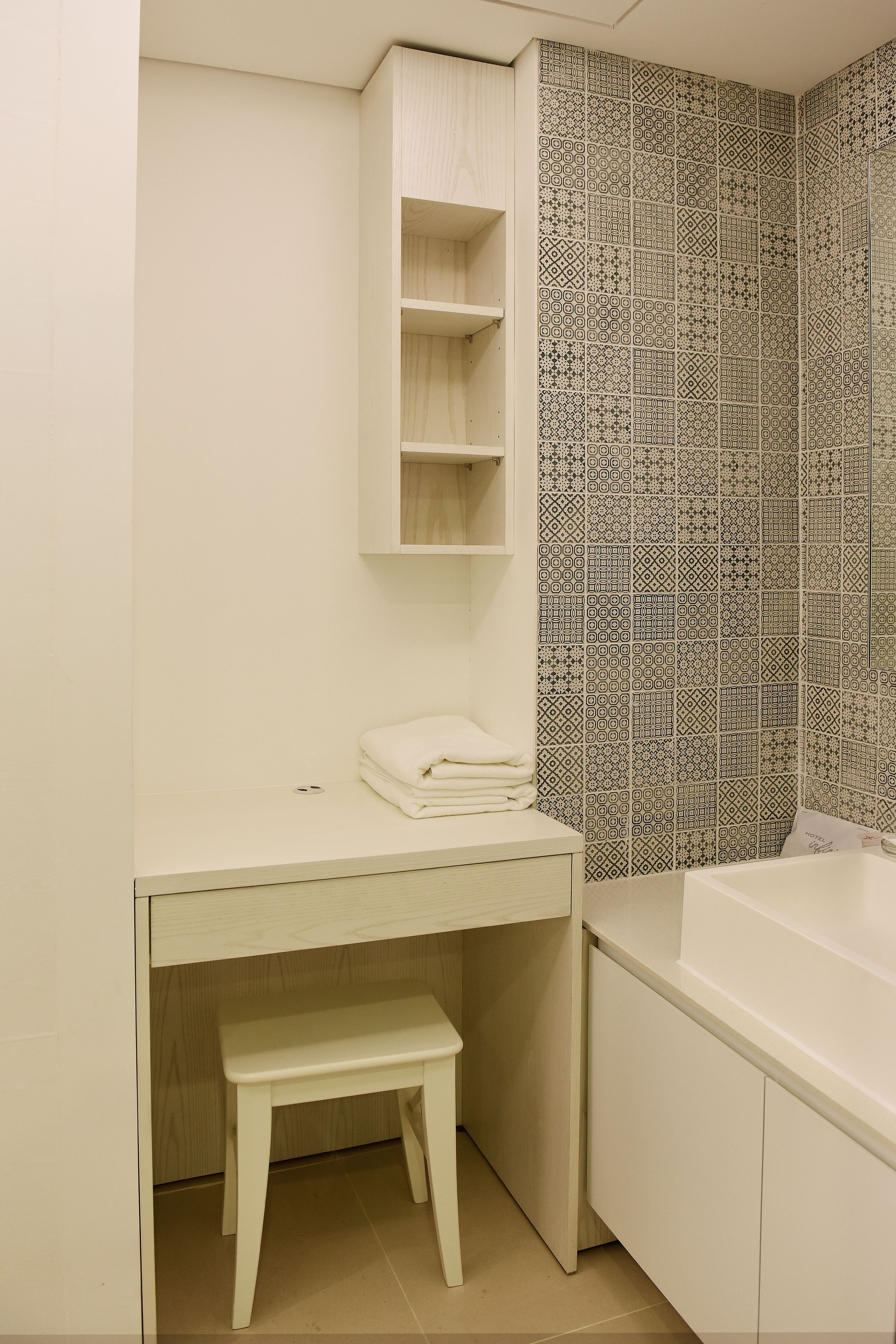 A bathroom with a white vanity, a sink, a mirror, a towel rack, and a patterned shower wall.