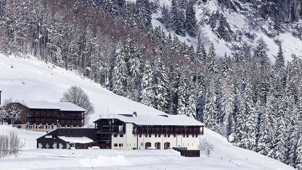 A snow-covered lodge with multiple buildings, surrounded by a forest and mountains.