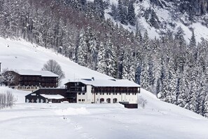 A snow-covered lodge with multiple buildings, surrounded by a forest and mountains. - Hôtel Club Le Risoux (Bois-d'Amont)