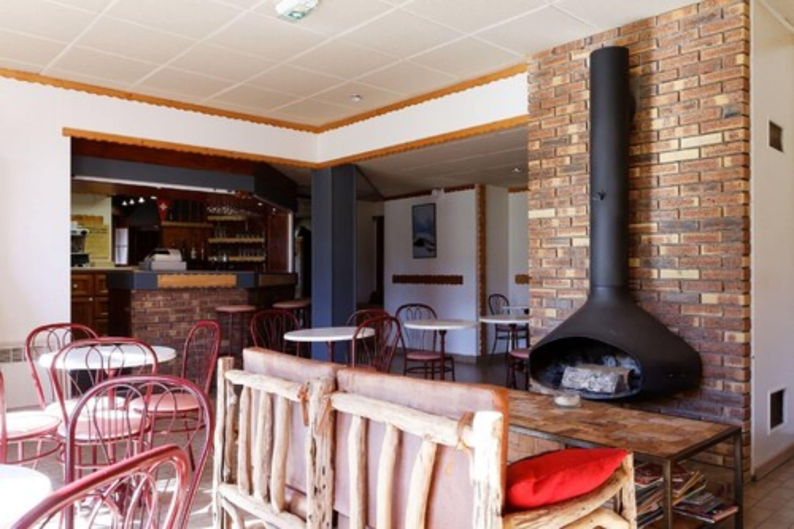 A restaurant with brick walls, a large black chimney, and red metal chairs.