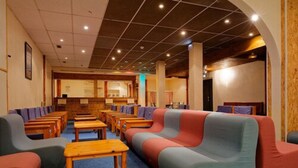 A hotel lobby with rows of seating, a reception desk, and a wooden ceiling.