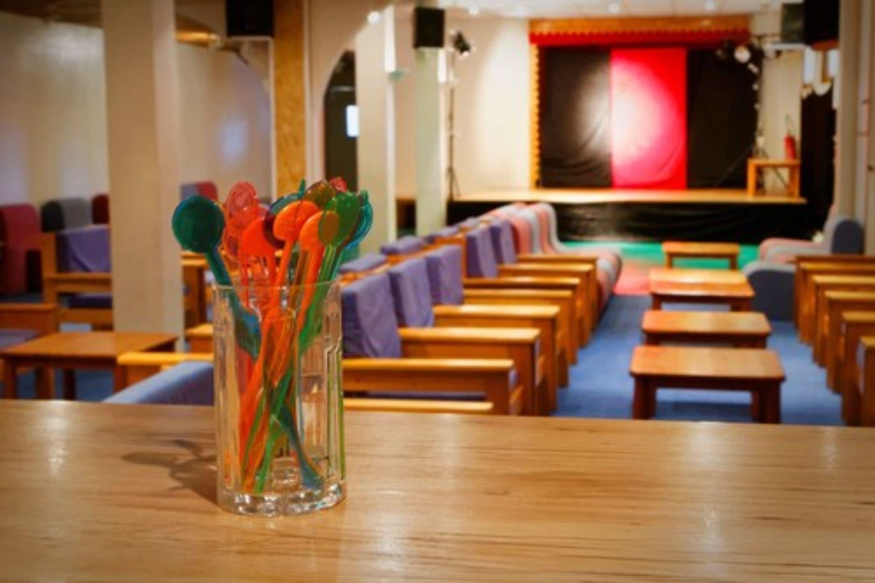 A church interior with pews arranged in rows, a stage with a red backdrop, and a clear glass vase with colorful items on a table.