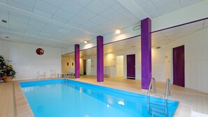 An indoor swimming pool with a blue water feature, surrounded by purple pillars and white walls.
