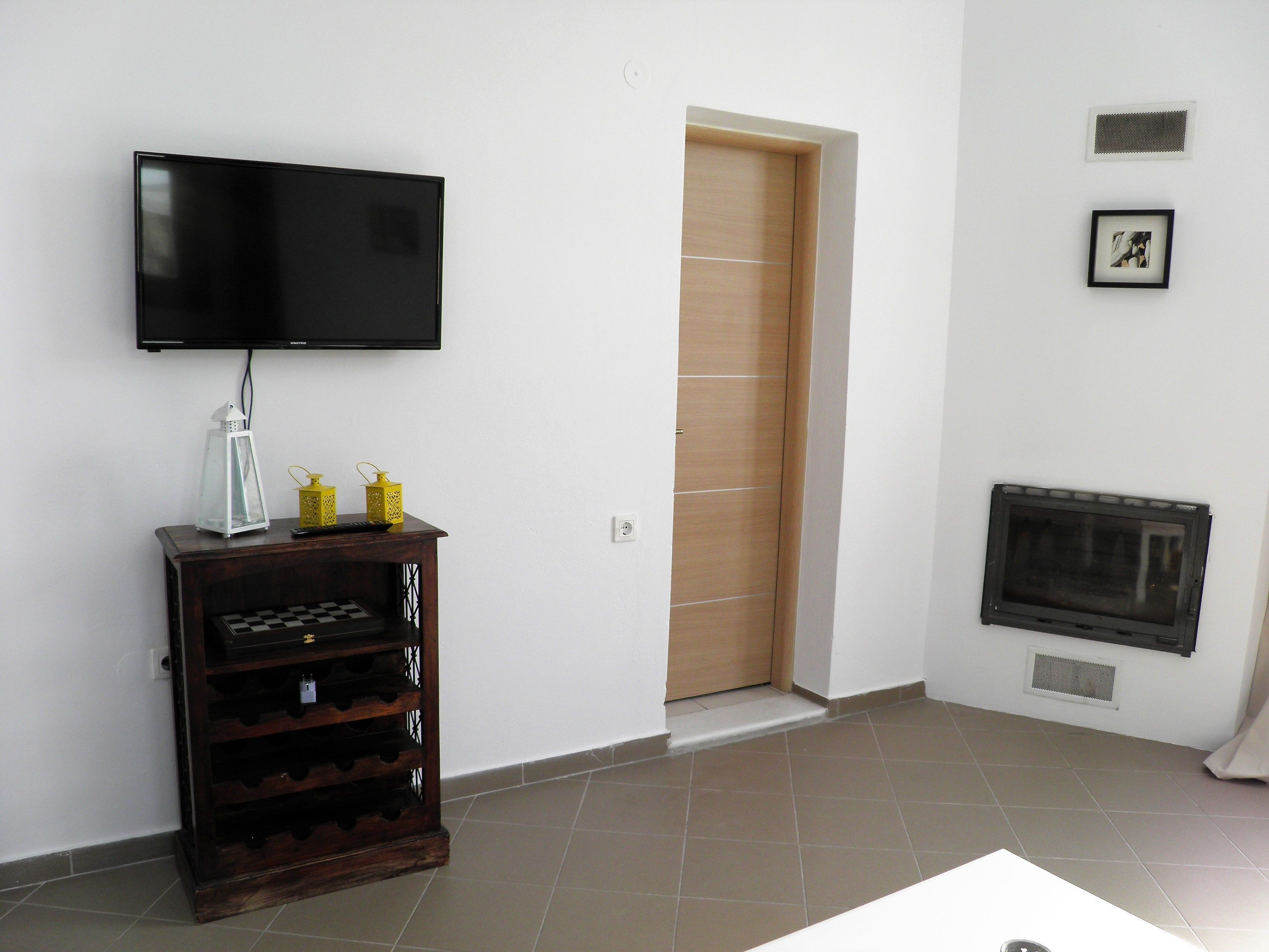 Una sala de estar con un televisor de pantalla plana montado en la pared, un botellero de madera, una chimenea y una puerta de madera.