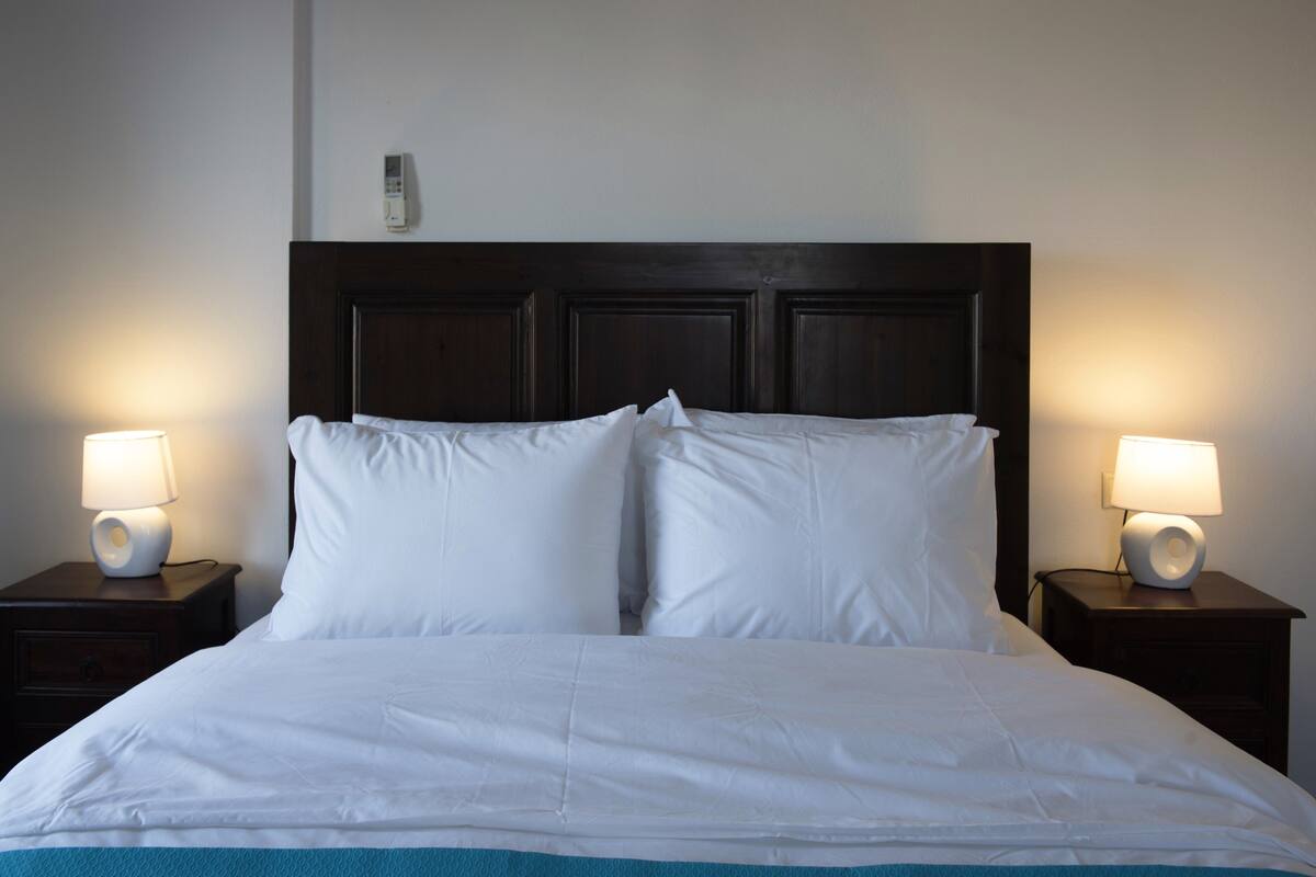 A neatly made bed with white linens and a dark headboard, flanked by two bedside tables with lamps.