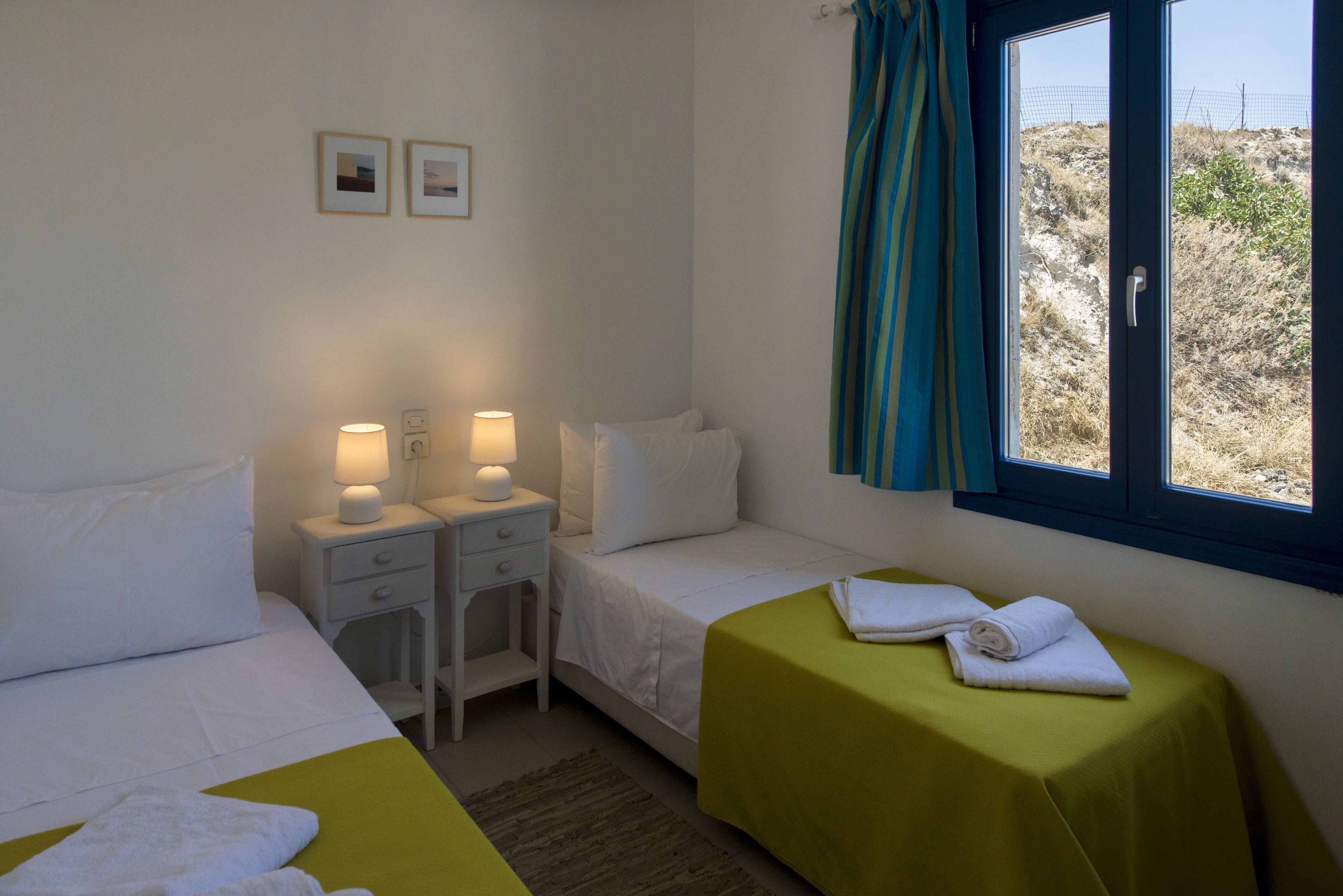 A hotel room with two beds, a window with curtains, and a small table with lamps.