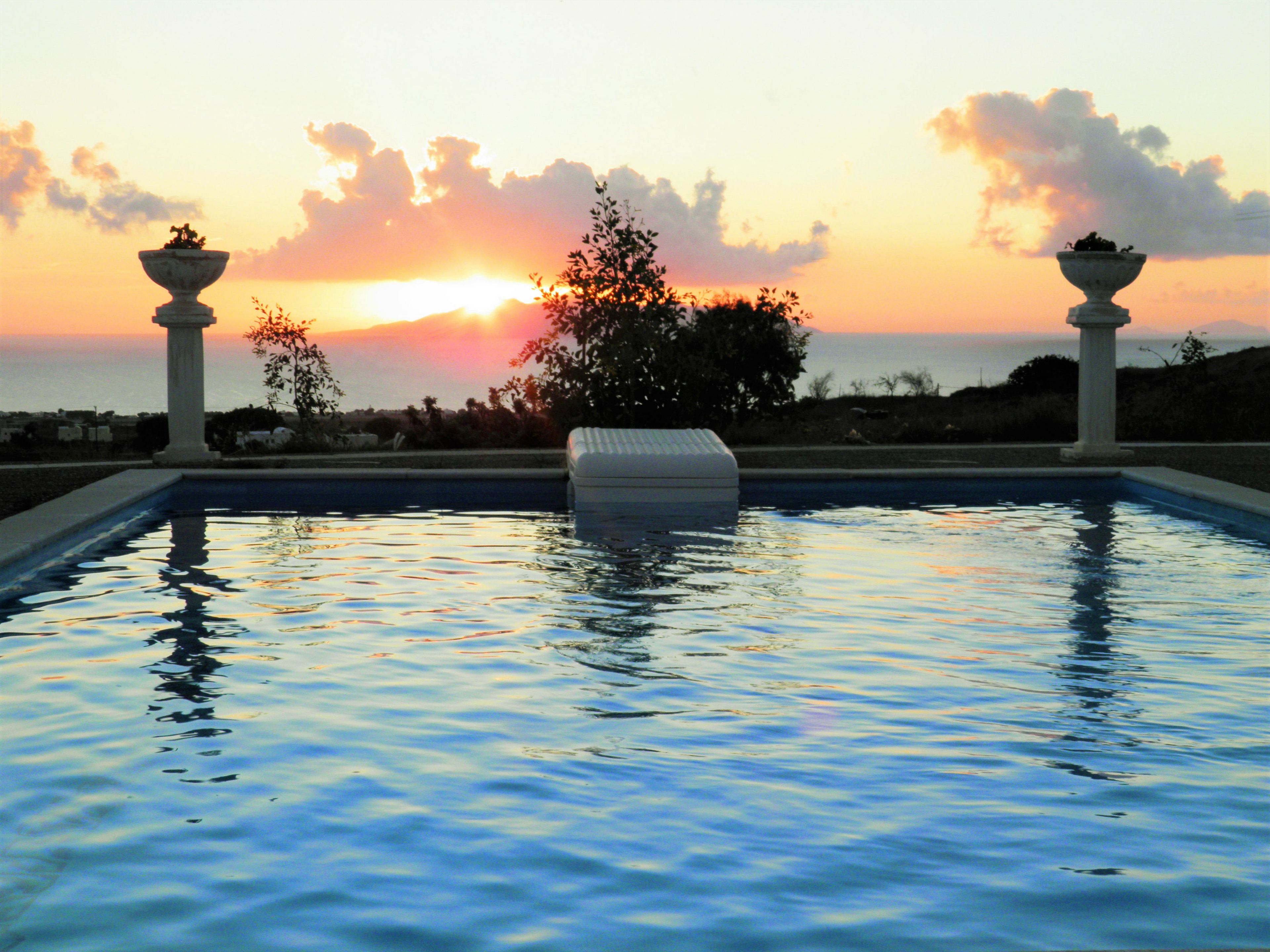 Una piscina con vistas a un atardecer, rodeada de columnas y un árbol.