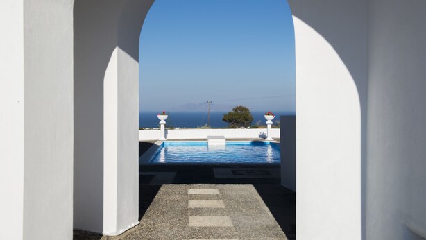 A pool area with a clear view of the sea through an archway. - Santorini Traditional Suites (Santorini)