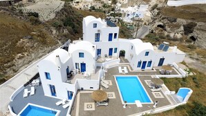 A white building with a swimming pool, outdoor seating, and a small garden area. - Santorini Traditional Suites (Santorini)