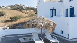A white building with blue accents, a thatched umbrella, and two white lounge chairs. - Santorini Traditional Suites (Santorini)