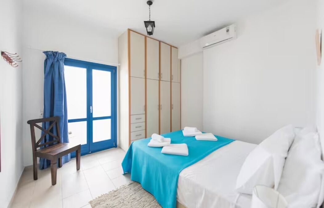 A bedroom with a bed, a wardrobe, a chair, and a window with curtains.