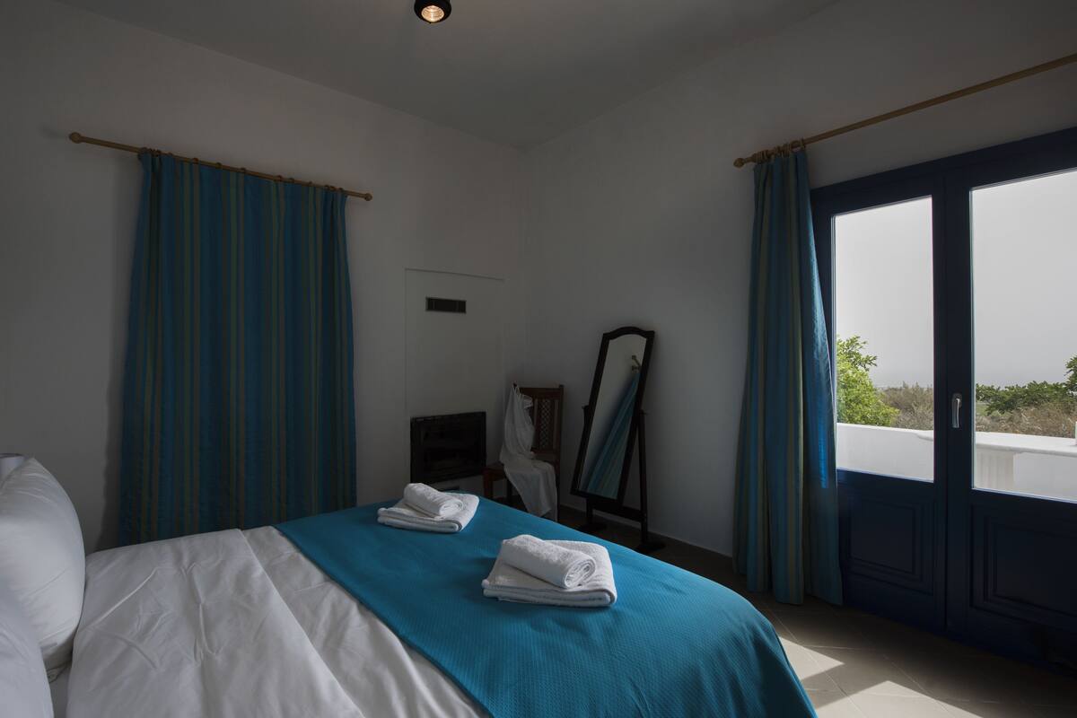A hotel room with a bed, a chair, a mirror, and a view of the outdoors.