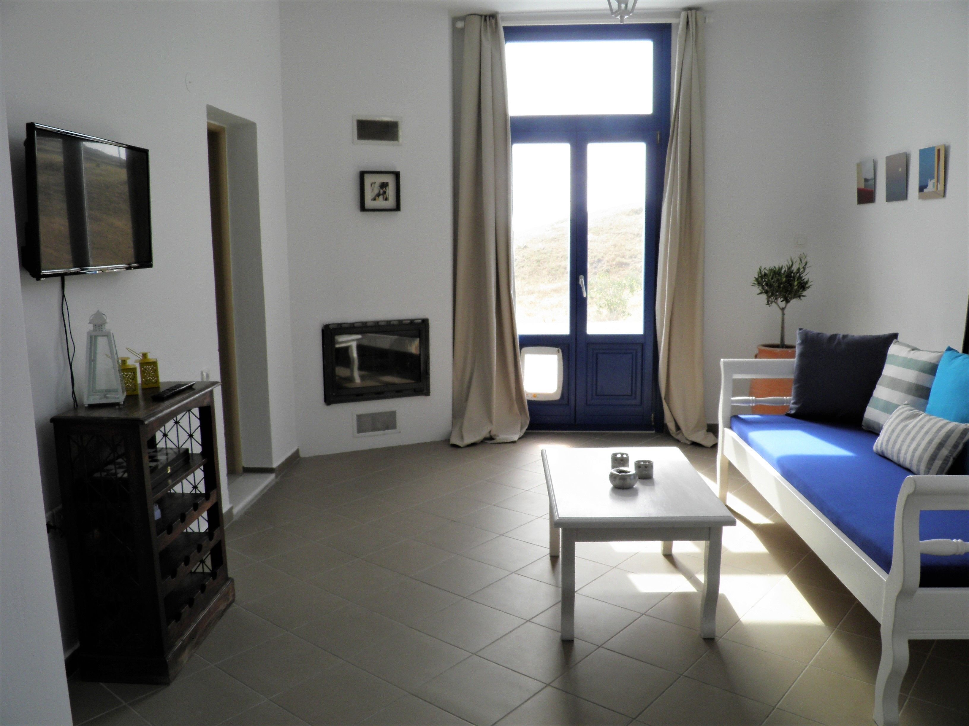 A living room with a white sofa, a coffee table, a TV mounted on the wall, and a window with curtains.