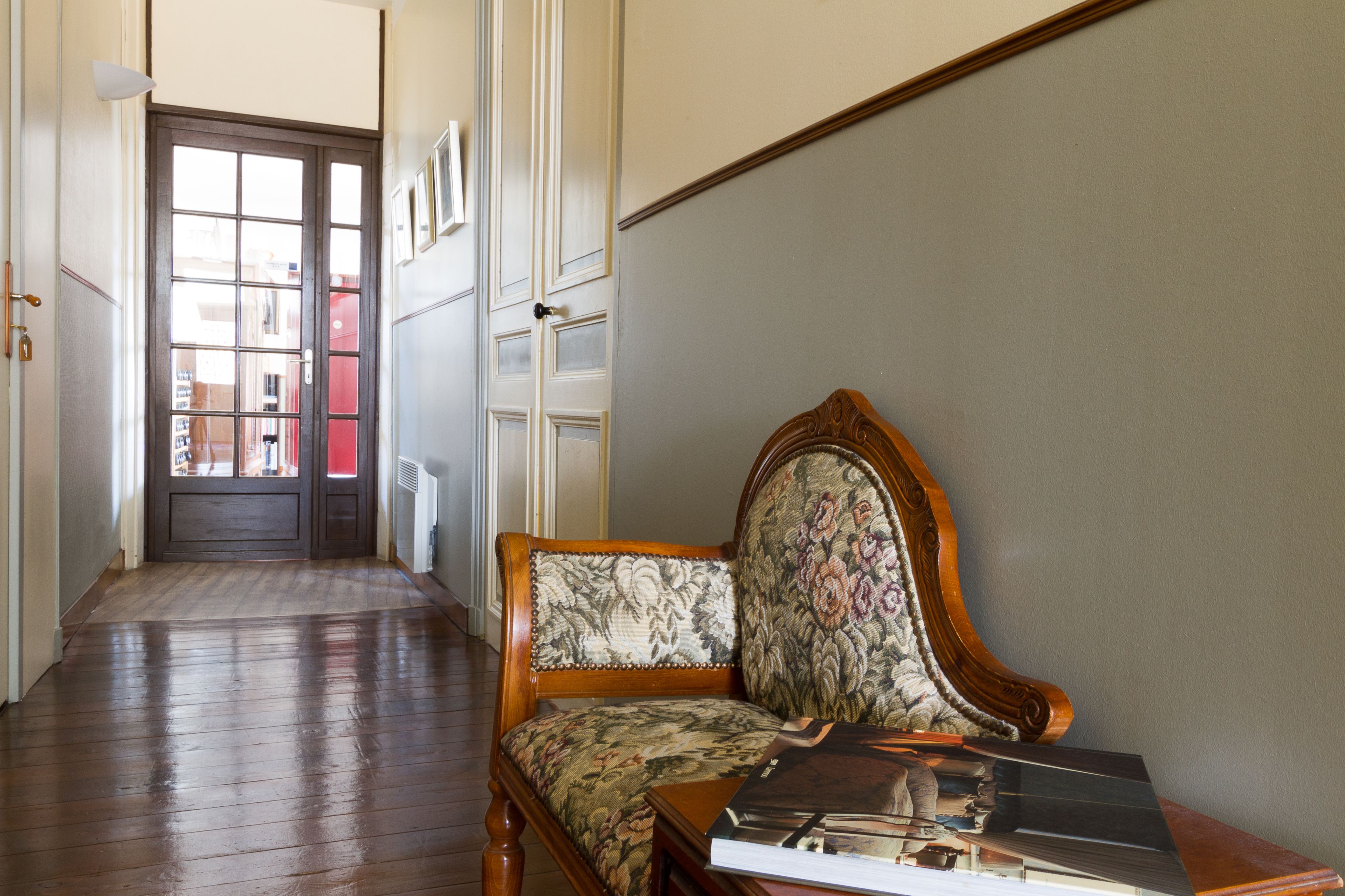 A hallway with a wooden floor, a door with glass panels, and a chair with a floral upholstery.