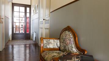 A hallway with a wooden floor, a door with glass panels, and a chair with a floral upholstery.