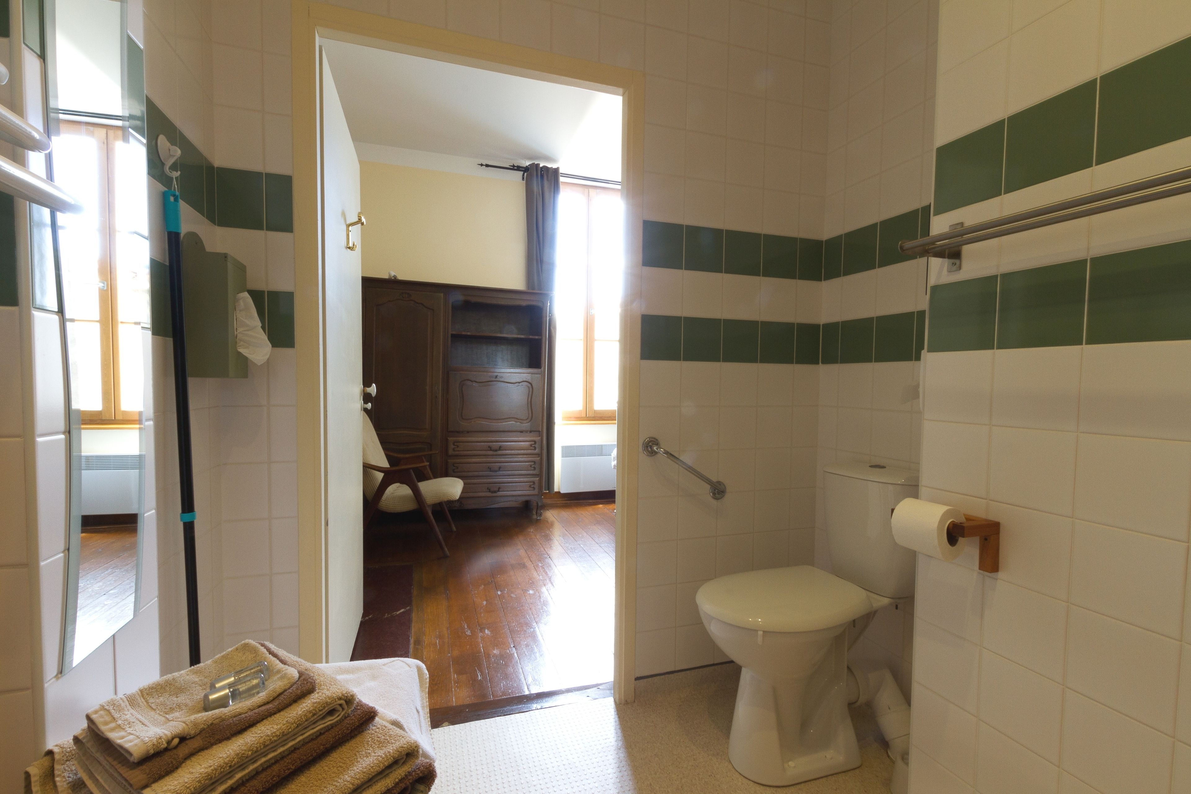 A bathroom with a toilet, a towel stack, and a wooden door leading to a bedroom.
