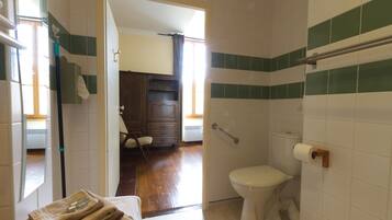 A bathroom with a toilet, a towel stack, and a wooden door leading to a bedroom.