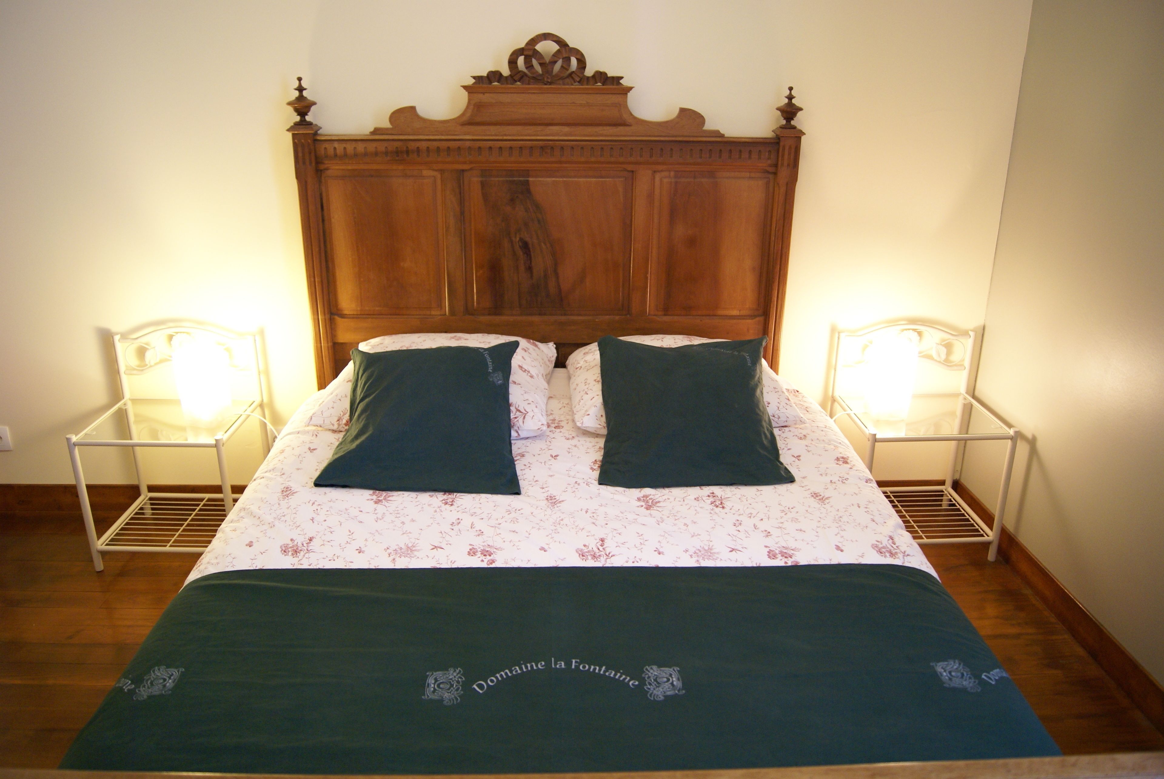 Een bed met een houten hoofdbord, twee nachtkastjes en een bloemenbedekking.