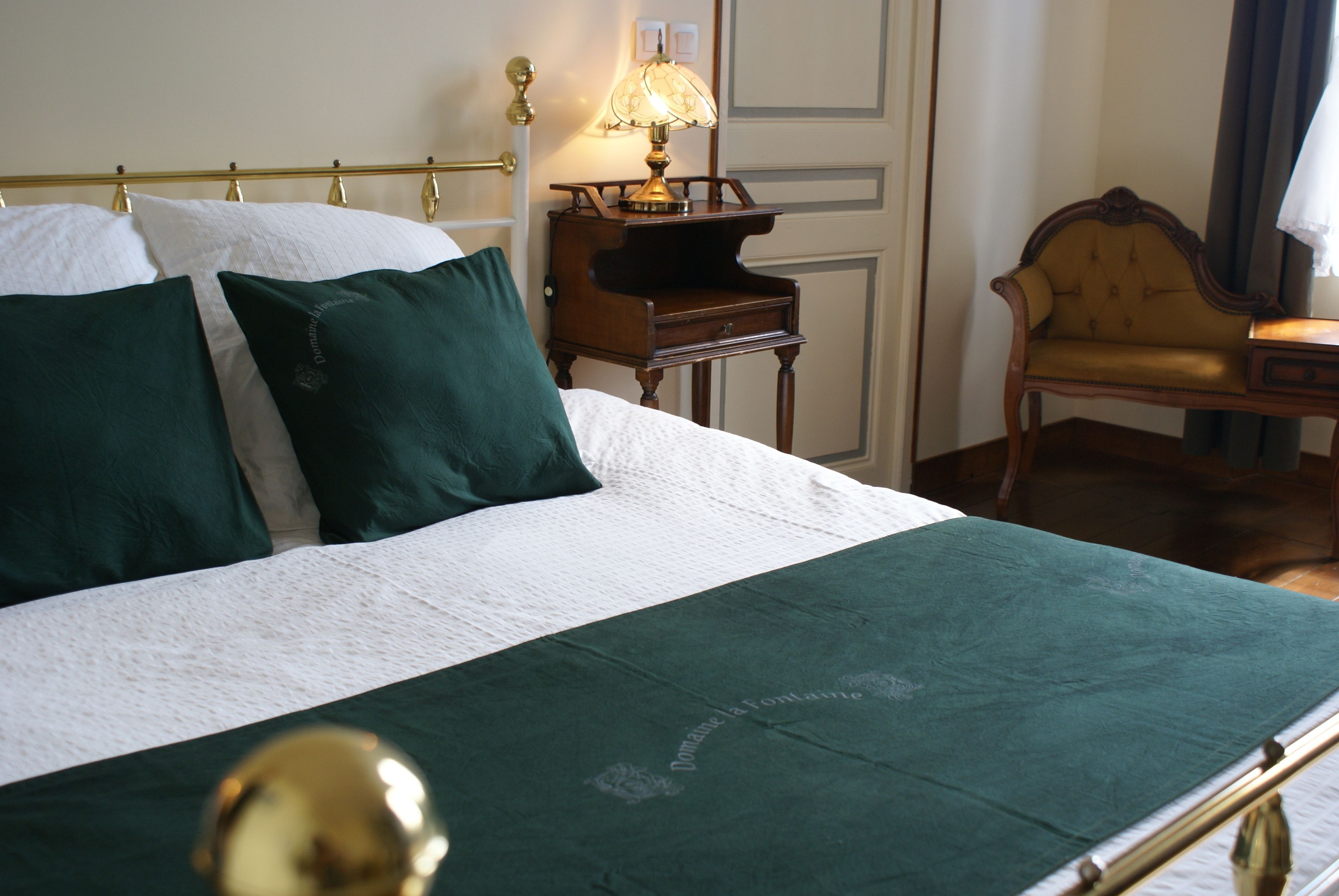 A neatly made bed with a white and green bedspread, a bedside table with a lamp, and a chair in a hotel room.