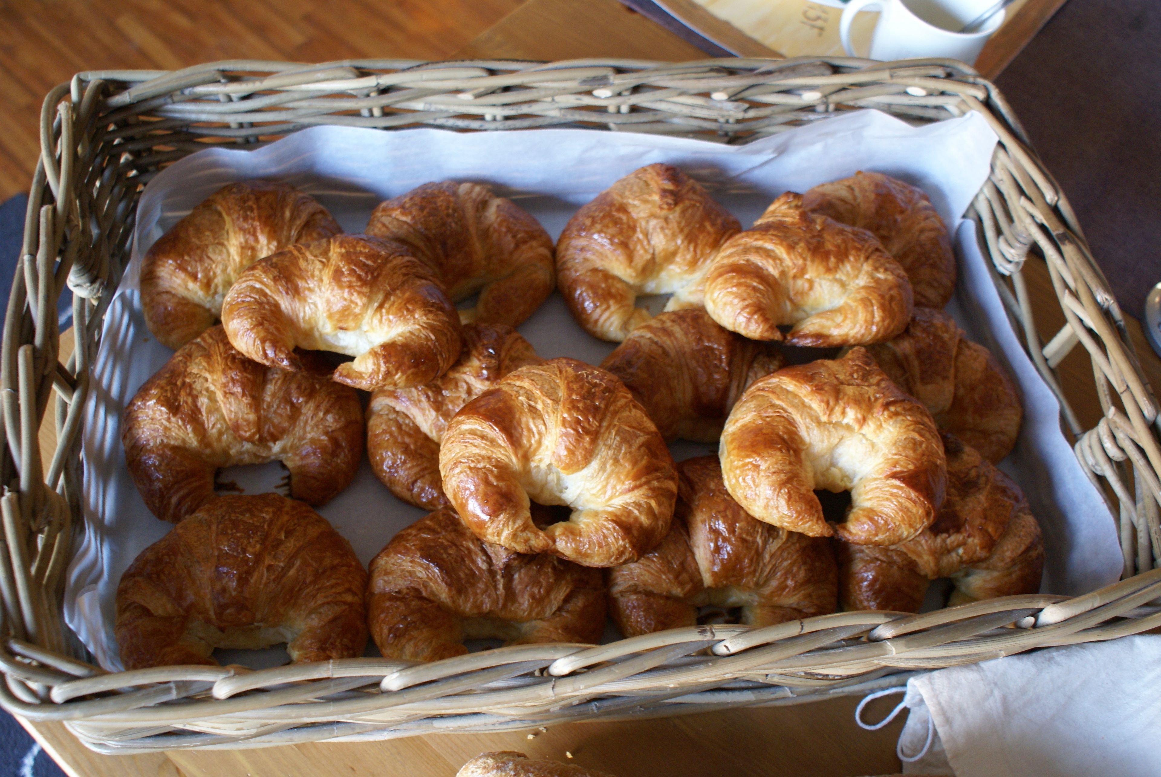 A wicker basket filled with golden-brown croissants on a wooden surface.